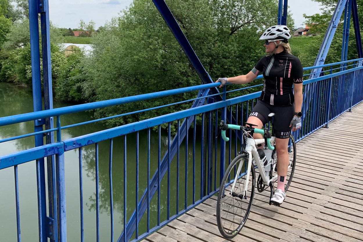 Rennradfahrerin h&auml;lt sich am Gel&auml;nder einen blauen Br&uuml;cke fest.
